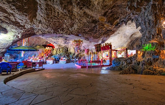 A wide cave chamber with shrines and altars beneath a rough limestone ceiling
